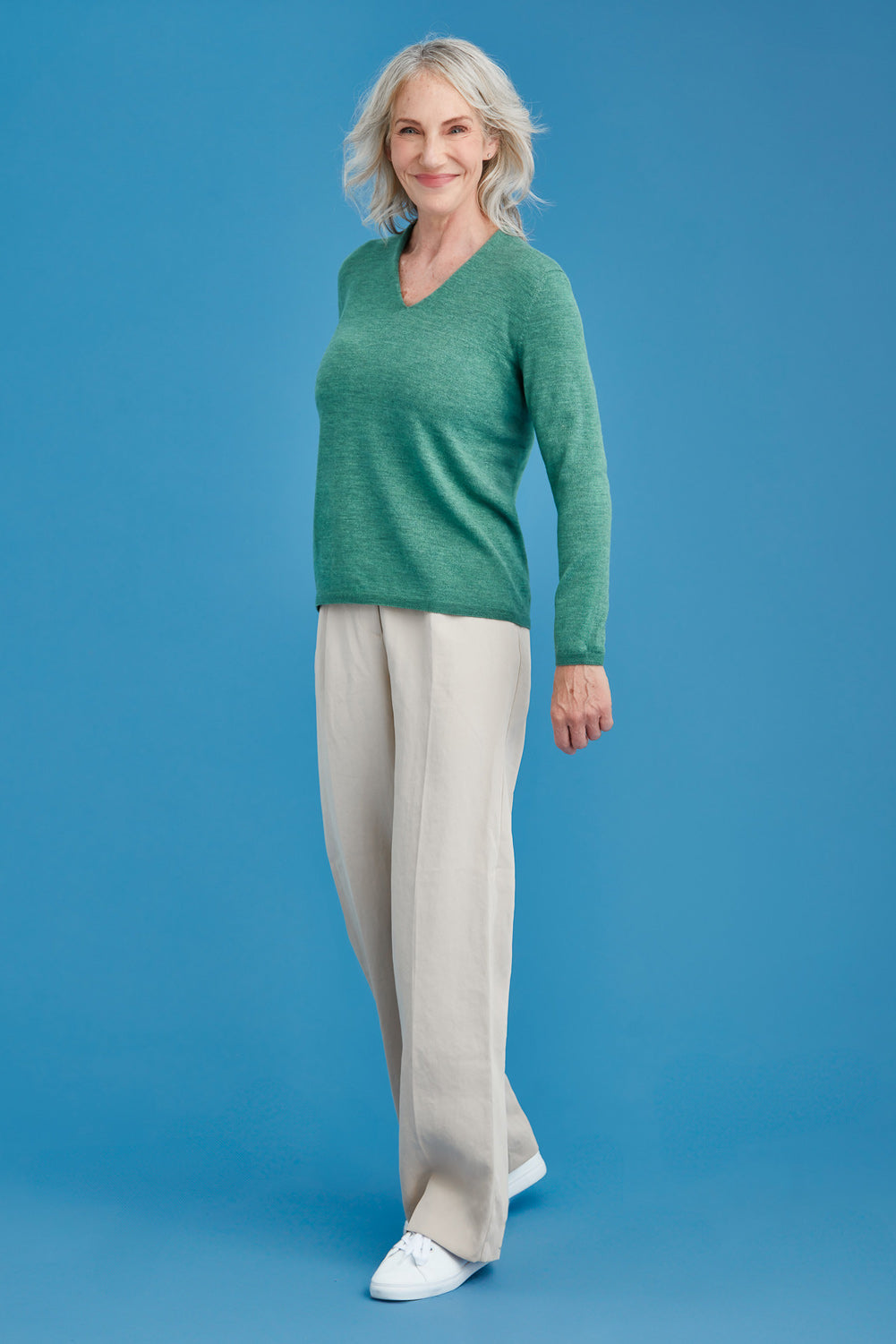 Woman wearing a green merino sweater against a blue background