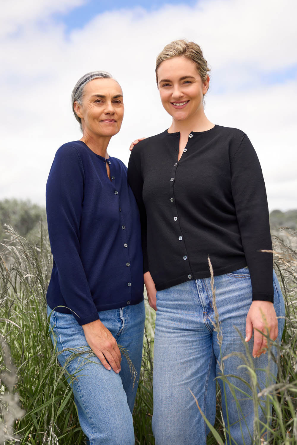 Two women standing outdoors, one wearing a navy blue button-down crew neck cardigan and the other in a black cardigan, both with button-up fronts.