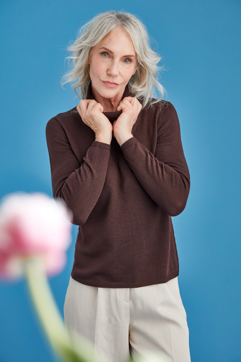 Woman wearing a brown polo sweater and beige pants against a blue background