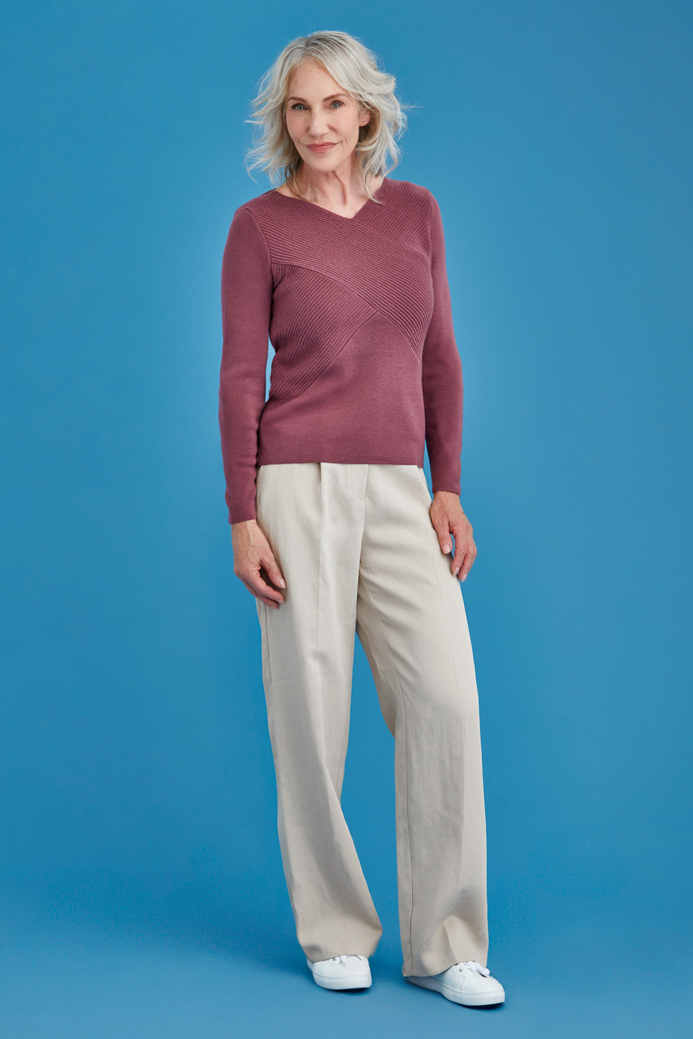 Woman wearing a mauve merino sweater and beige pants against a blue background