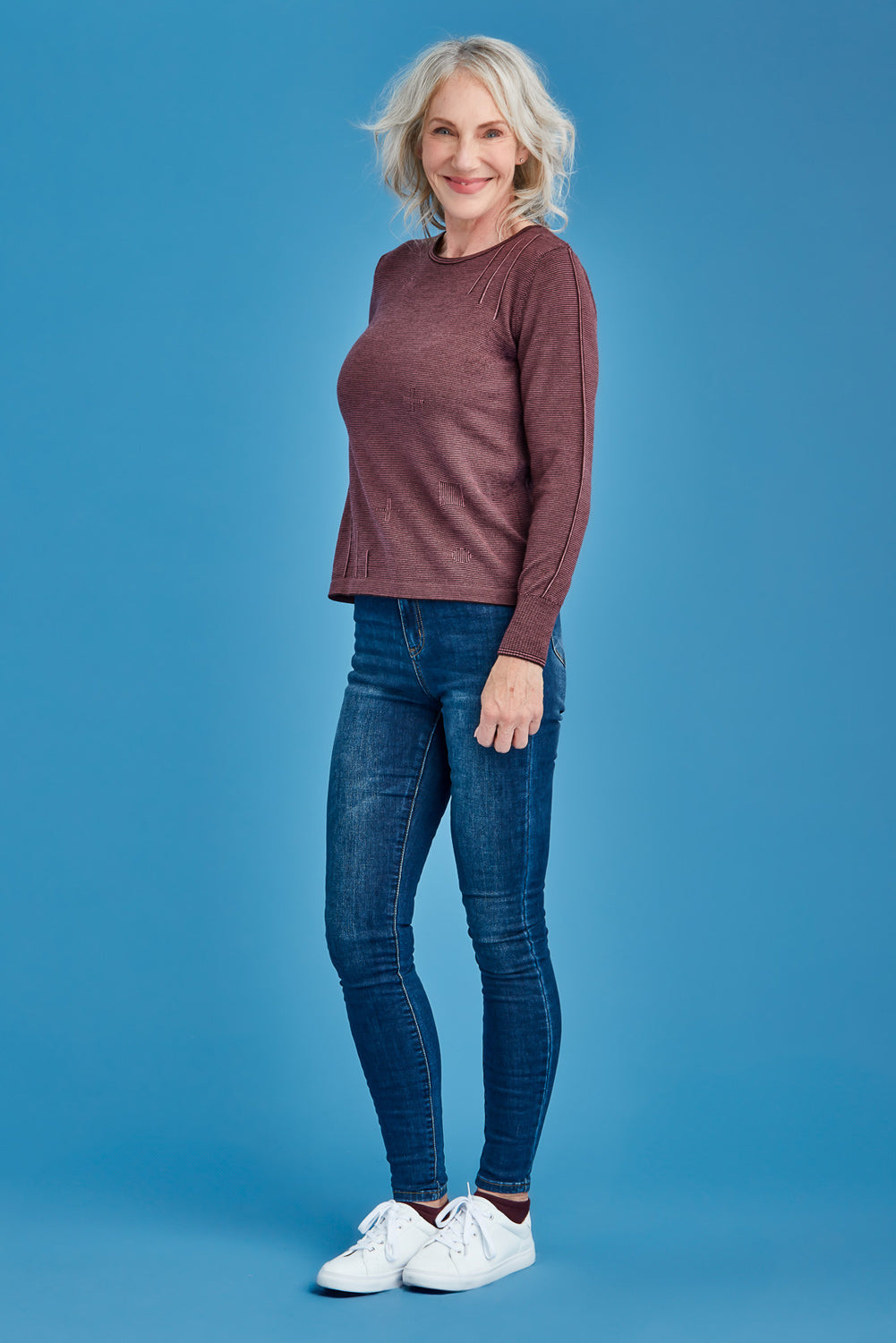 Woman wearing a mauve sweater, blue jeans, and white sneakers on a blue background
