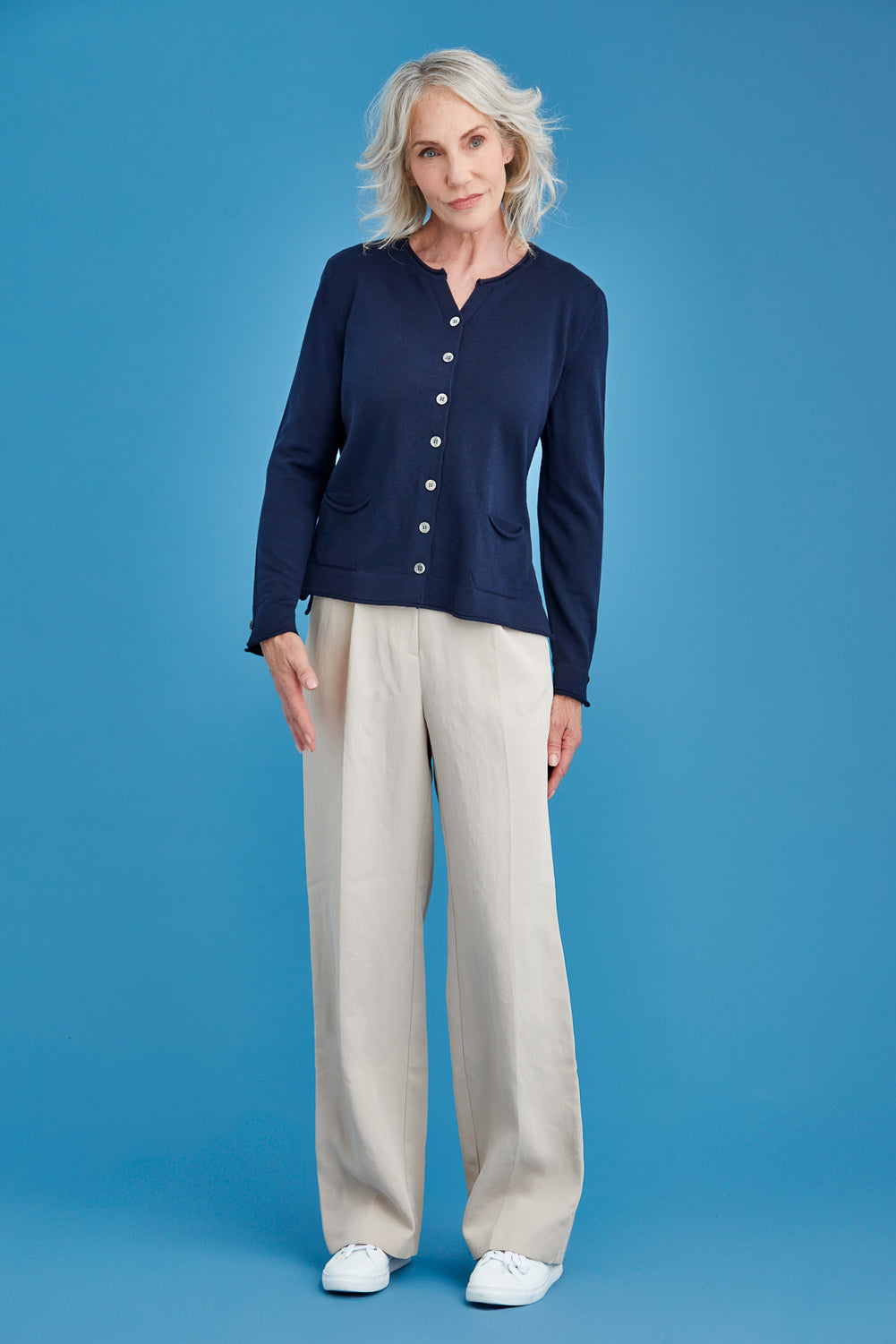 Woman wearing a navy cardigan and beige pants against a blue background