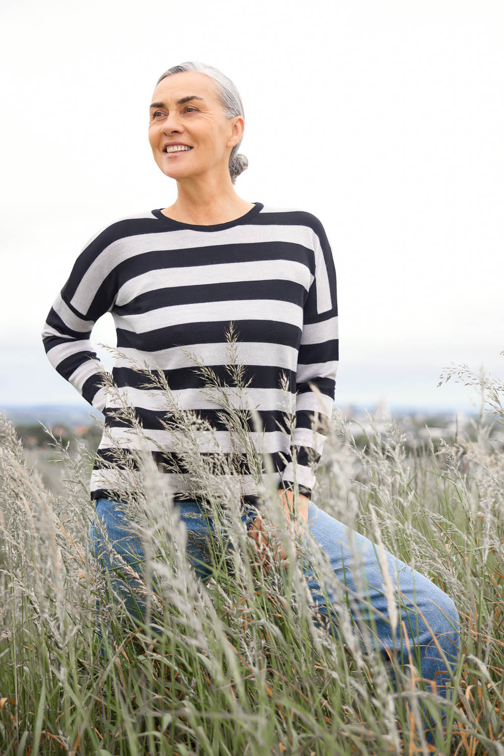 A woman standing outdoors wearing a grey and white striped drop shoulder jumper