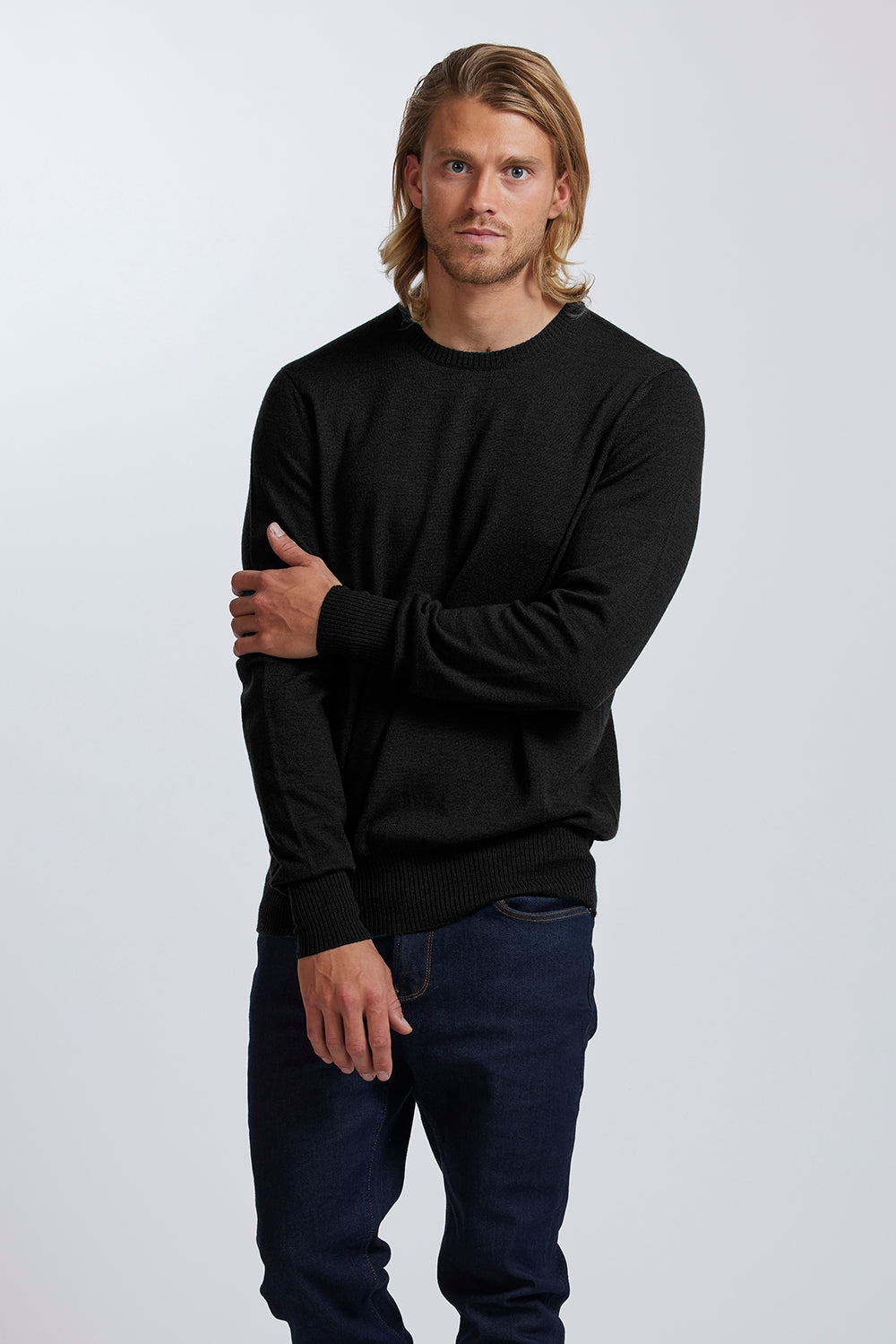 Man wearing a black sweater and jeans standing against a white background
