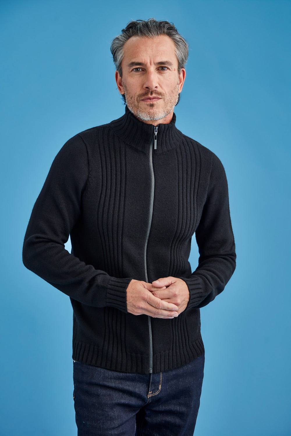 Man wearing a black zip-up sweater against a blue background