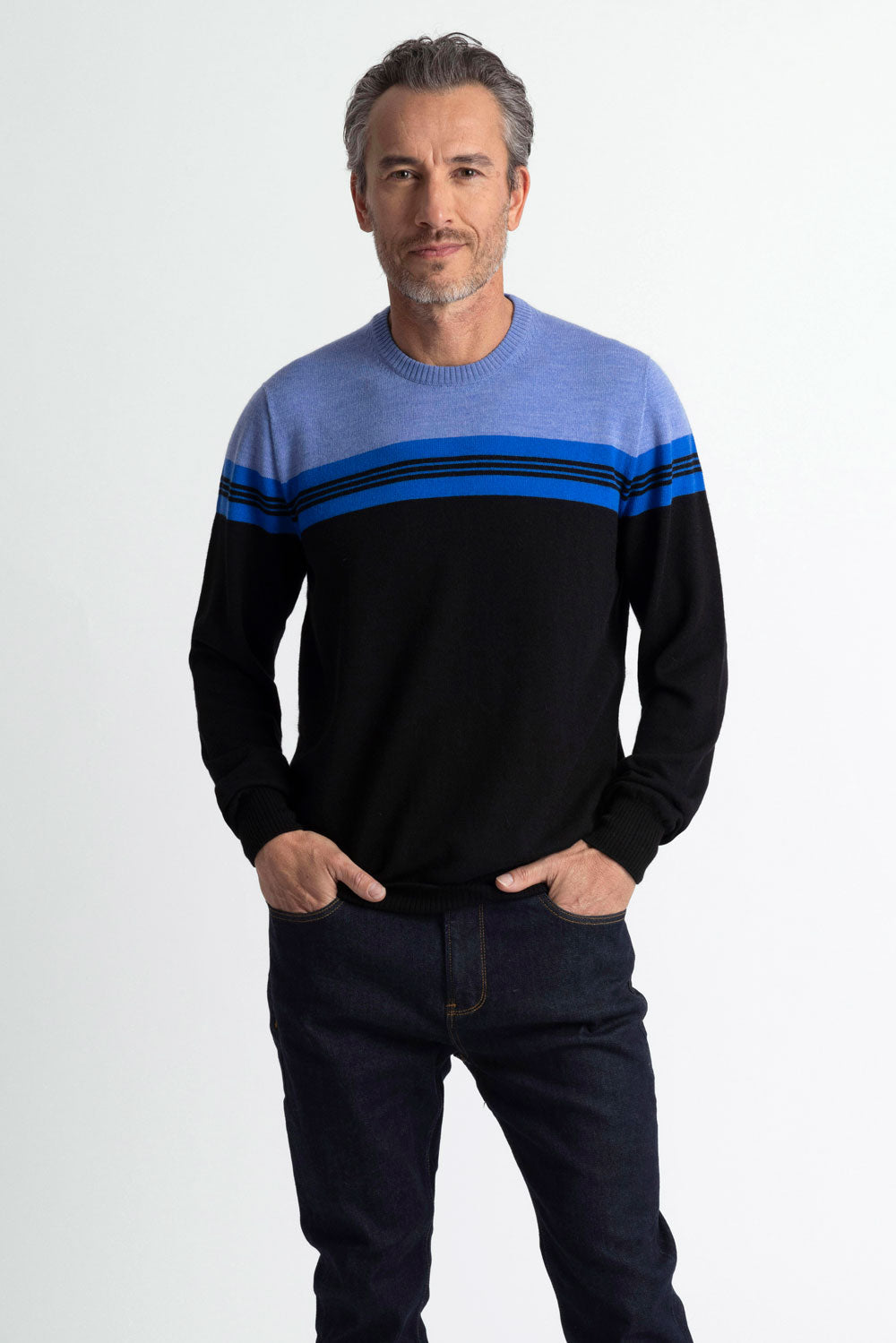A man wearing a navy blue and black variegated crew neck sweater and blue jeans.