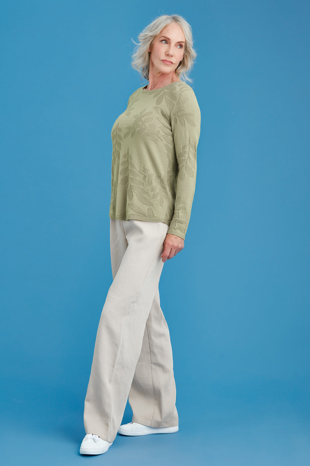 Woman wearing a light green top and beige pants against a blue background