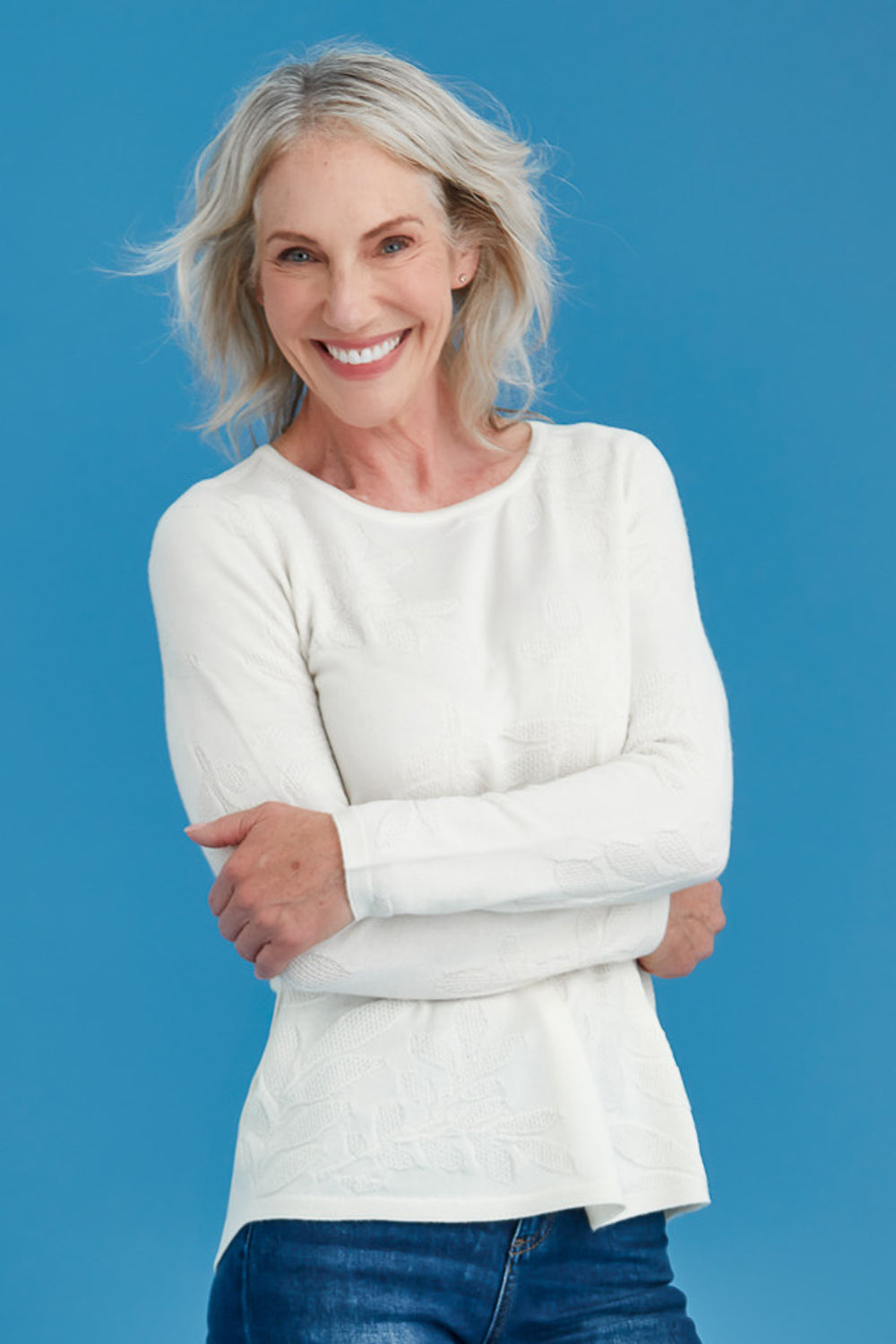 Woman wearing a white long-sleeve top against a blue background