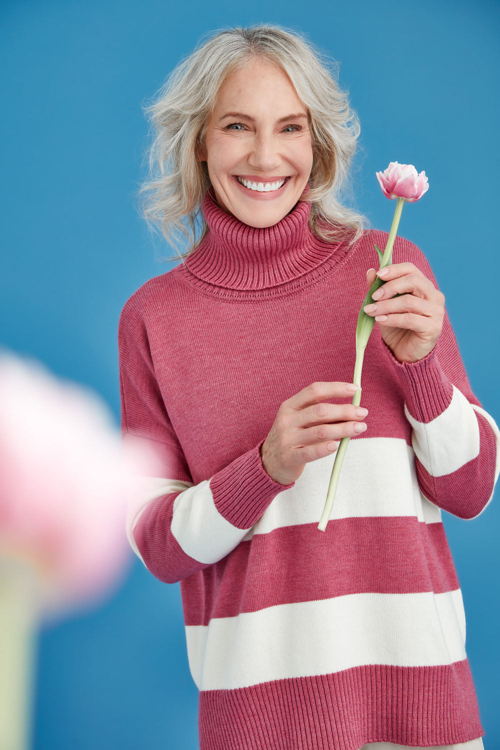 Woman wearing a pink and white striped sweater holding a flower against a blue background