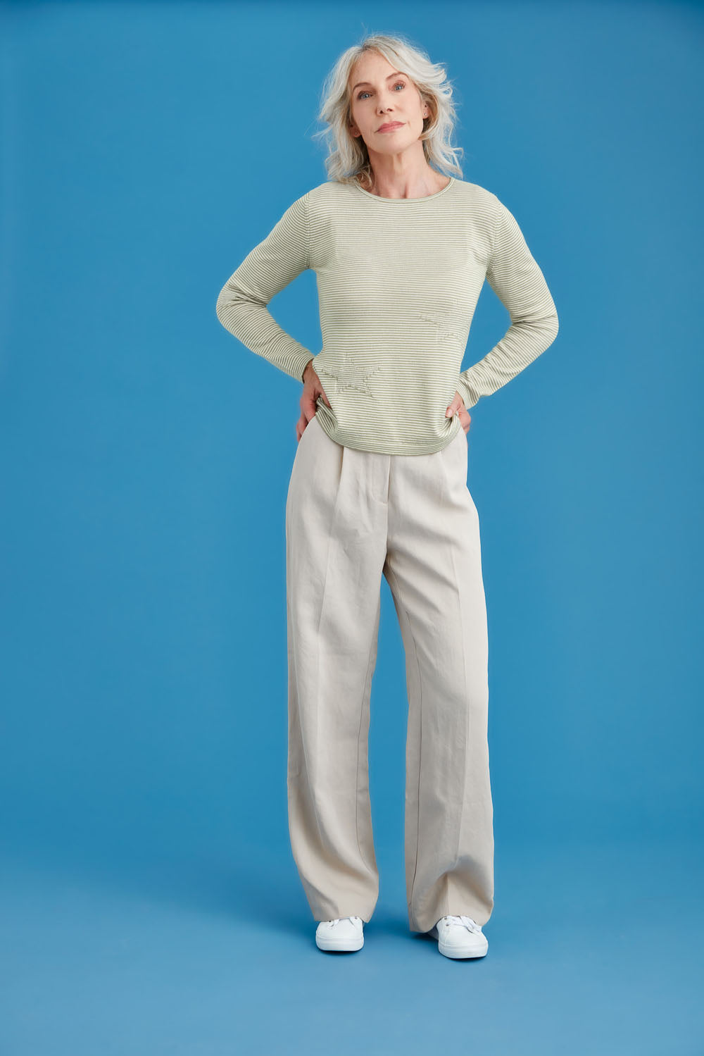 Woman wearing a light green striped merino sweater and blue jeans against a blue background