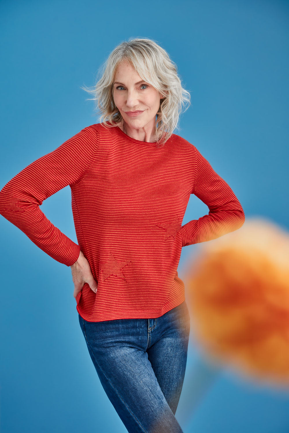 Woman wearing a red striped merino sweater and blue jeans against a blue background