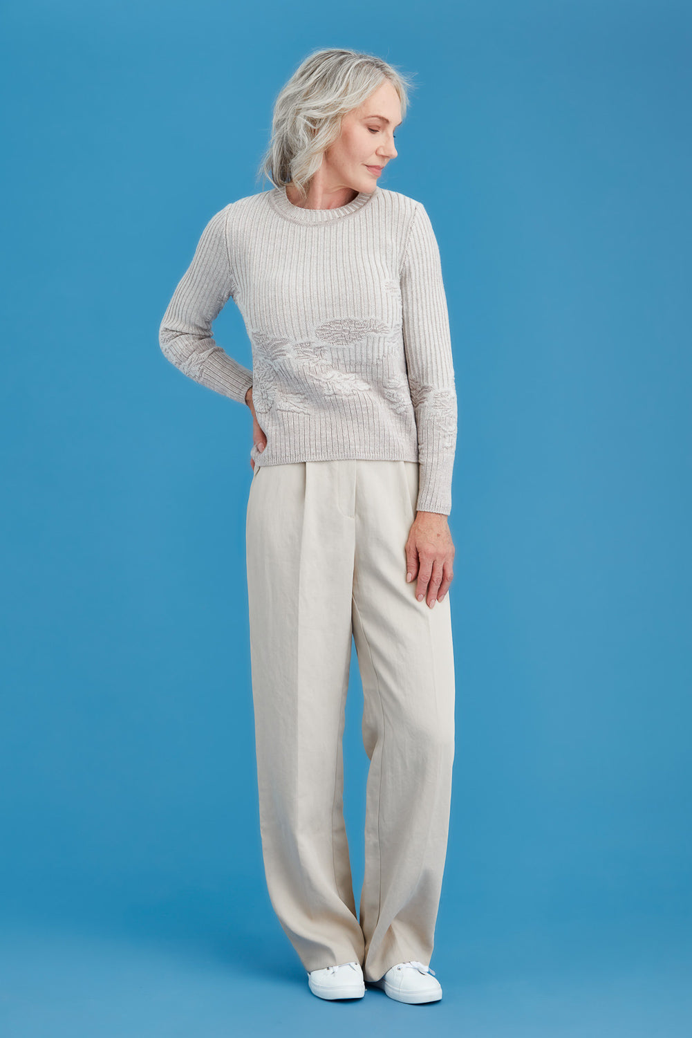 Woman wearing a light tan sweater with a floral pattern against a blue background