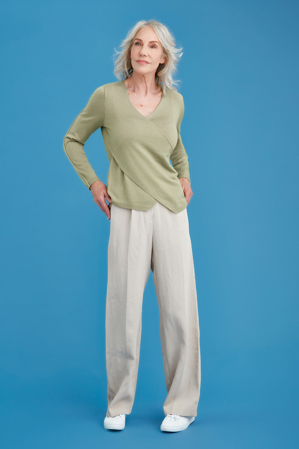 Woman wearing a green merino sweater and beige pants on a blue background