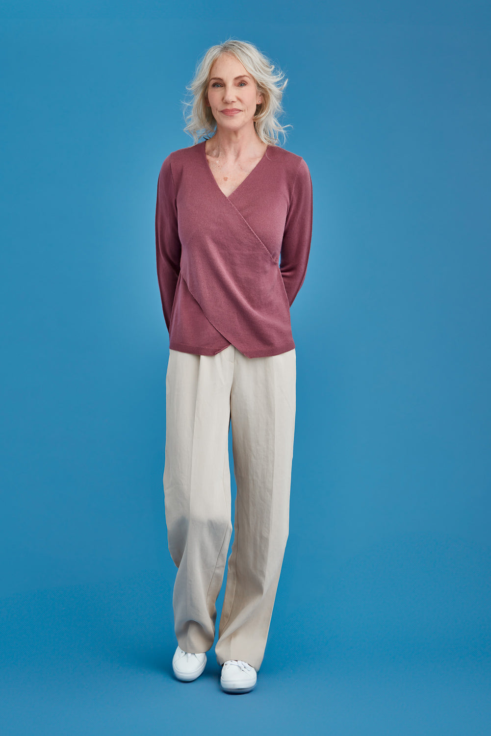 Woman wearing a mauve top and beige pants against a blue background